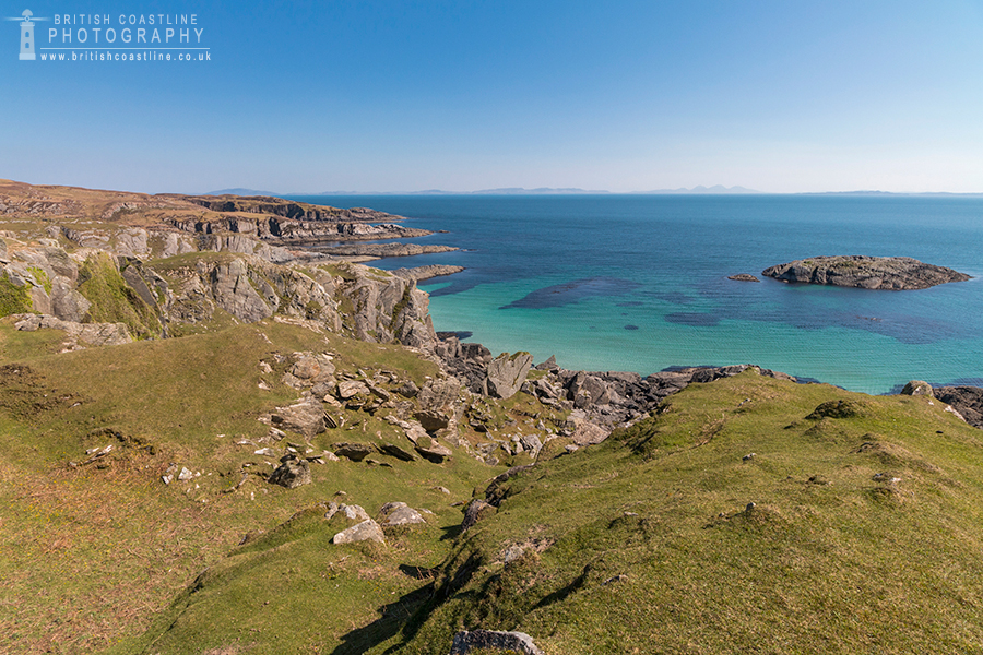 Isle of Mull coast, rocky strips of land going intio the turqoise sea with a distant Isle of Jura on the horizon