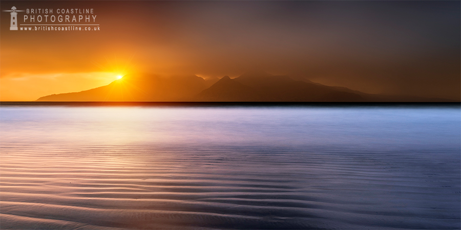 laig bay with ripples of sand in the foreground capturing the golden light with the indigo sea and a mountainous island with clouds brushhing the moutain tops