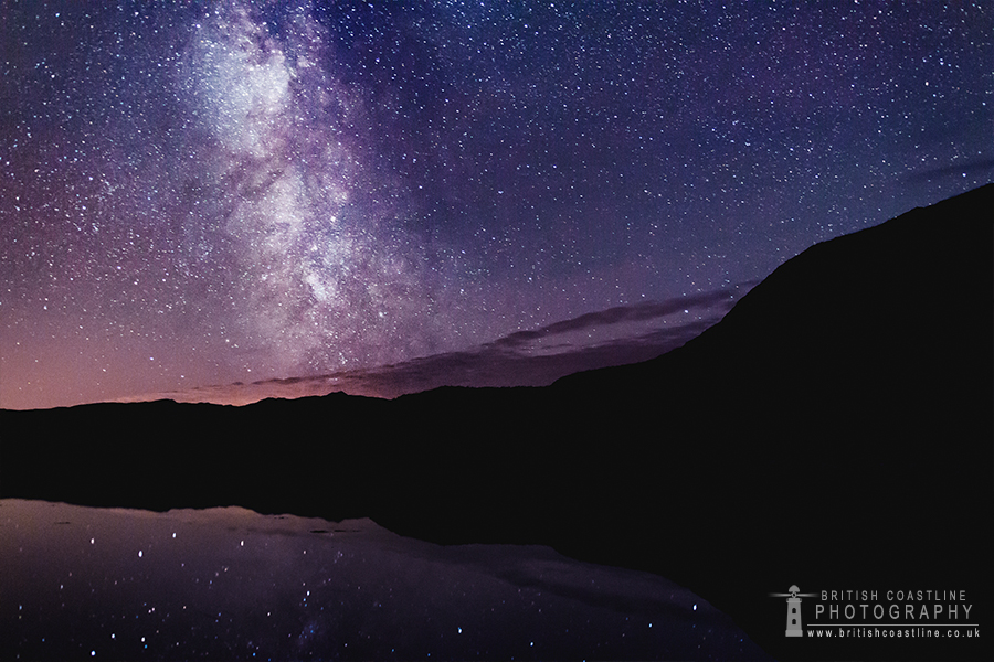 Milky Way, clear night sky, silhouetted sea cliffs, reflective sea loch